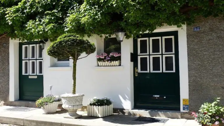 Porte d’entrée et volets en bois poncés et repeints sur une façade de maison rénovée, avec marquise en fer forgé