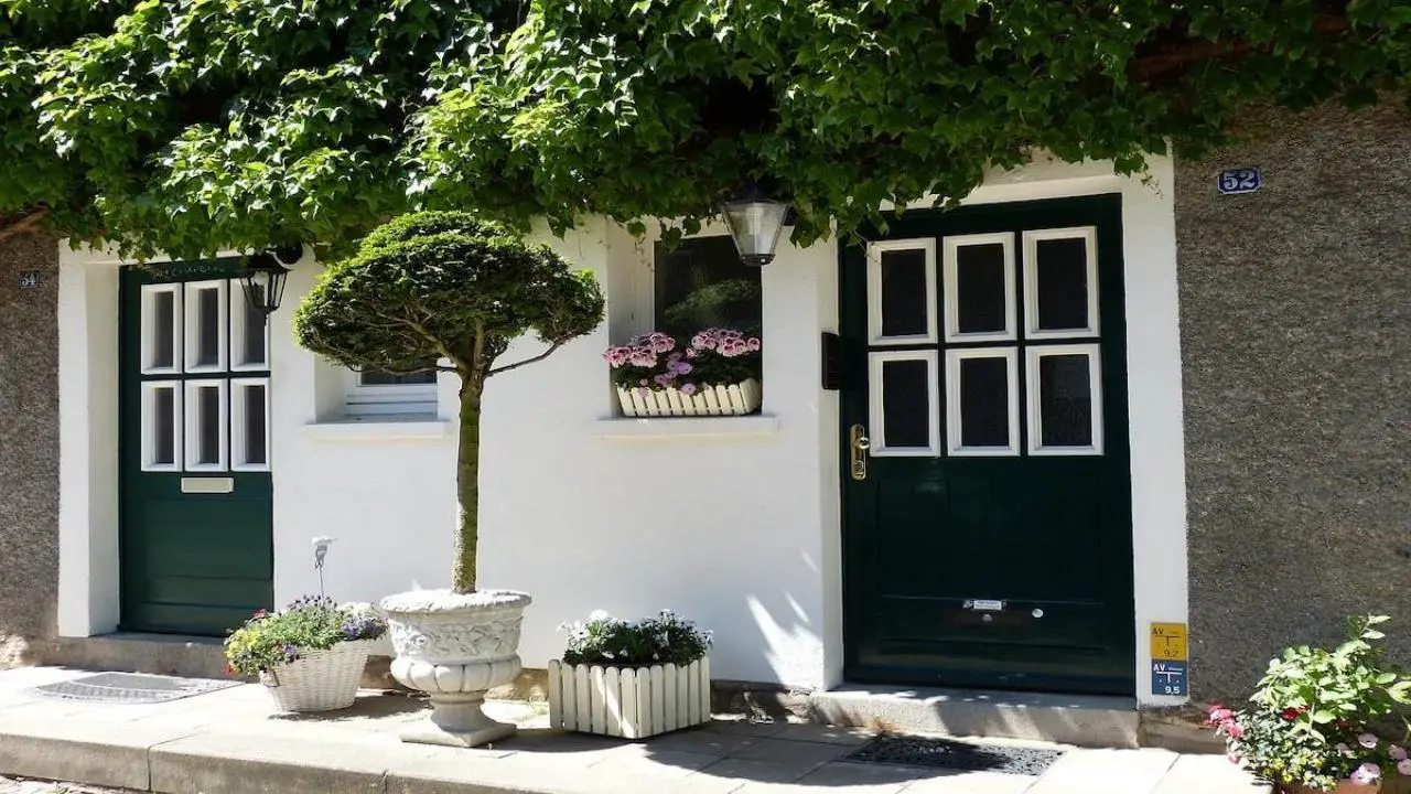 Porte d’entrée et volets en bois poncés et repeints sur une façade de maison rénovée, avec marquise en fer forgé